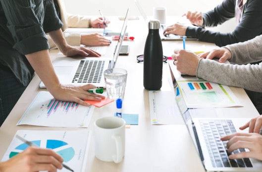 Team collaborating on eCommerce Digital Marketing Kick Starter Plan with laptops, charts, and analytics reports on a meeting table. Ideal for business setup.